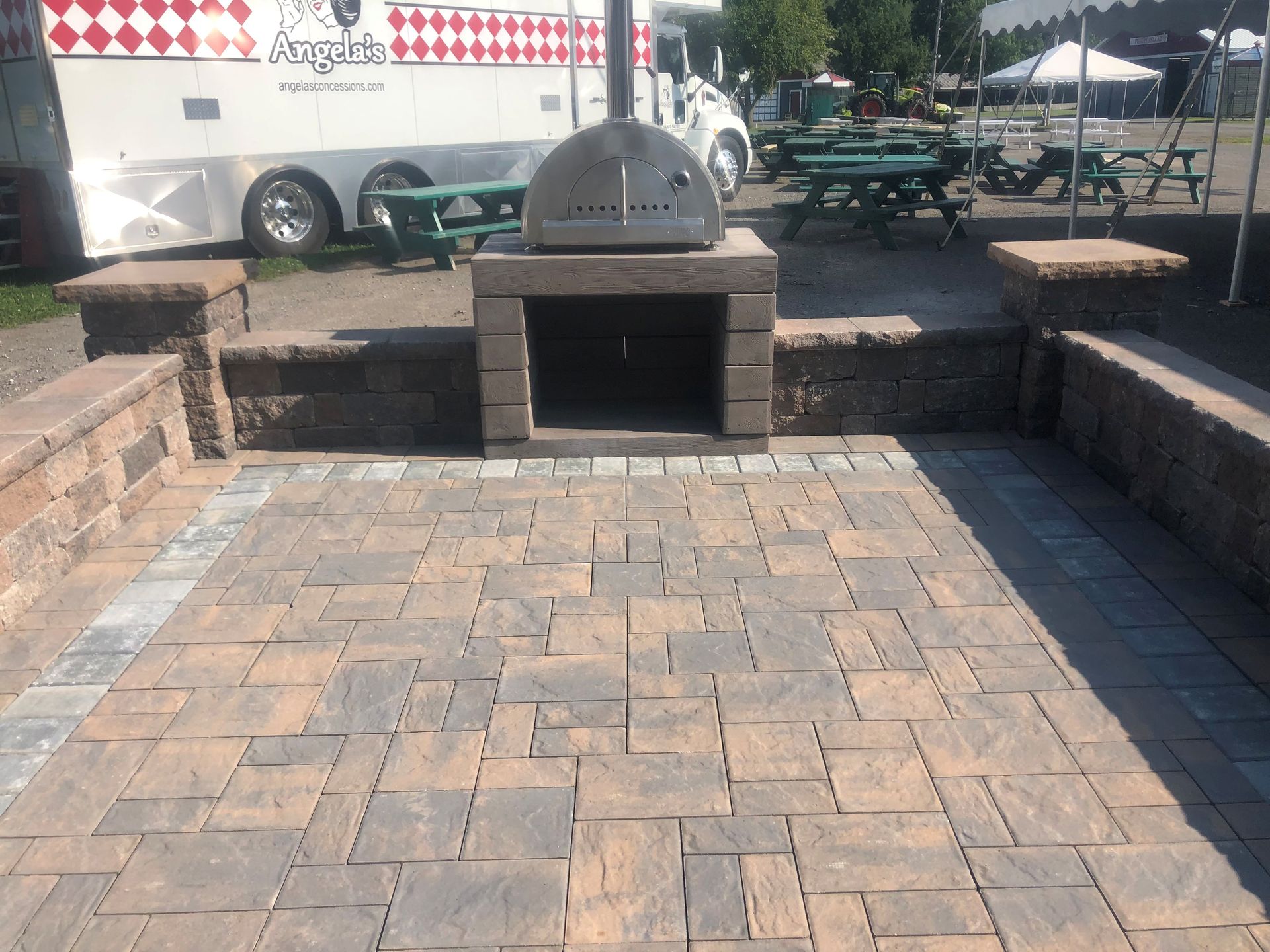A pizza oven is sitting on a brick patio next to a food truck