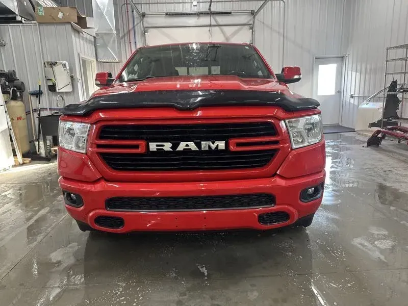 Red Ram pickup truck facing forward in a garage, with black hood protector.