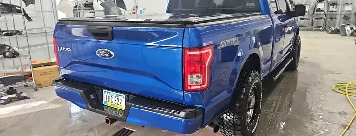 Blue Ford F-150 pickup truck with black wheels and a black bed cover in a workshop.