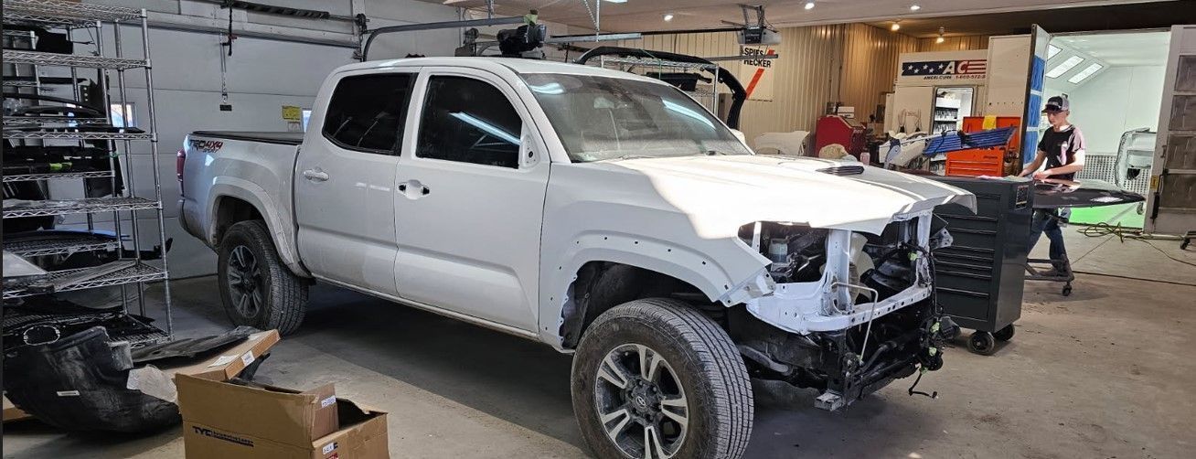 White pickup truck in a garage; front end disassembled. People working in the background.