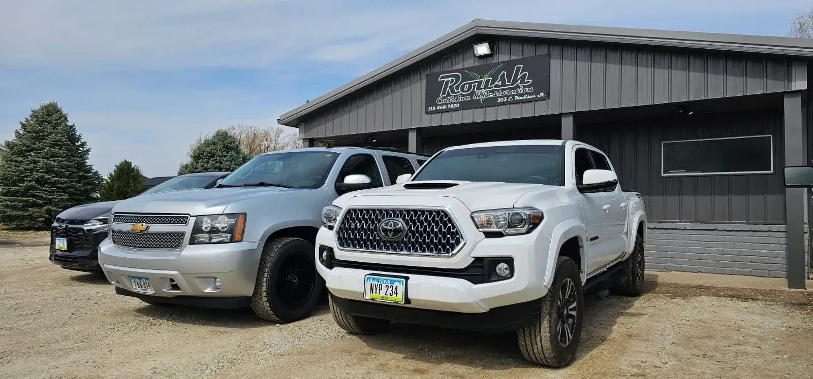 Three trucks parked in front of a gray building with a sign. The sky is blue.