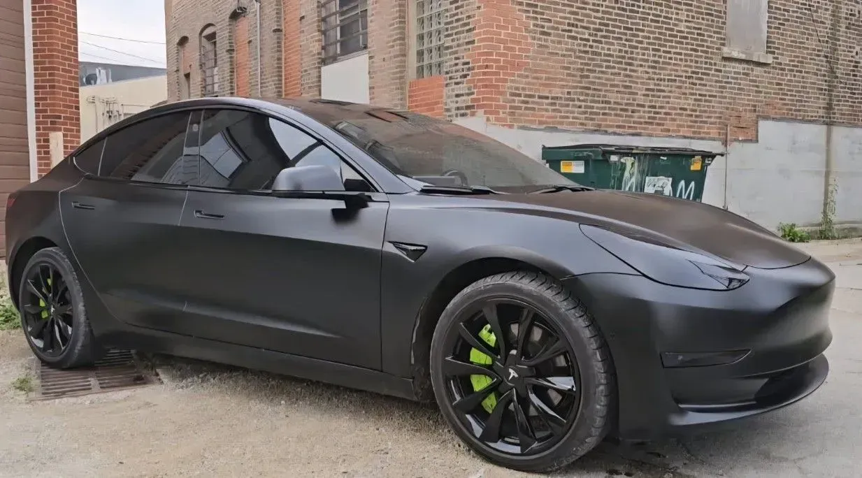 Black Tesla car with black wheels and lime green brake calipers parked in an alley.