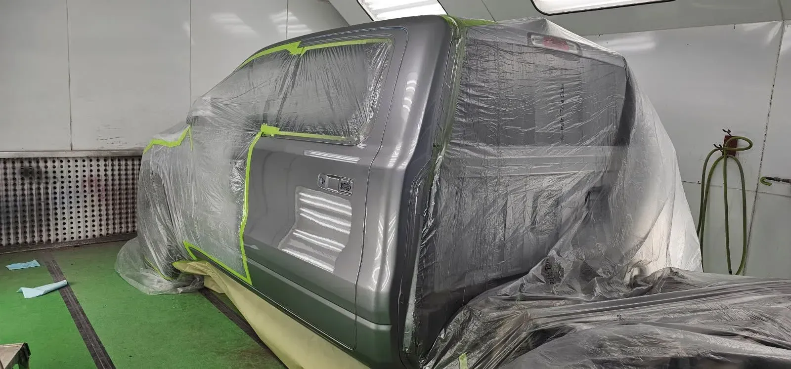 A pickup truck is in a paint booth covered in plastic and masking tape, ready for painting.