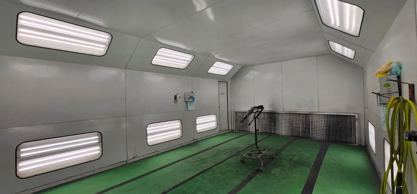 Interior of a spray paint booth with white walls, green floor, and overhead lights.