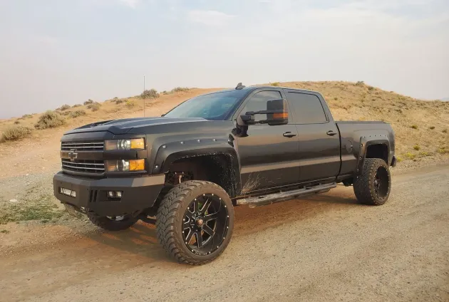 Black lifted pickup truck on a dirt road, parked on a desert hillside.