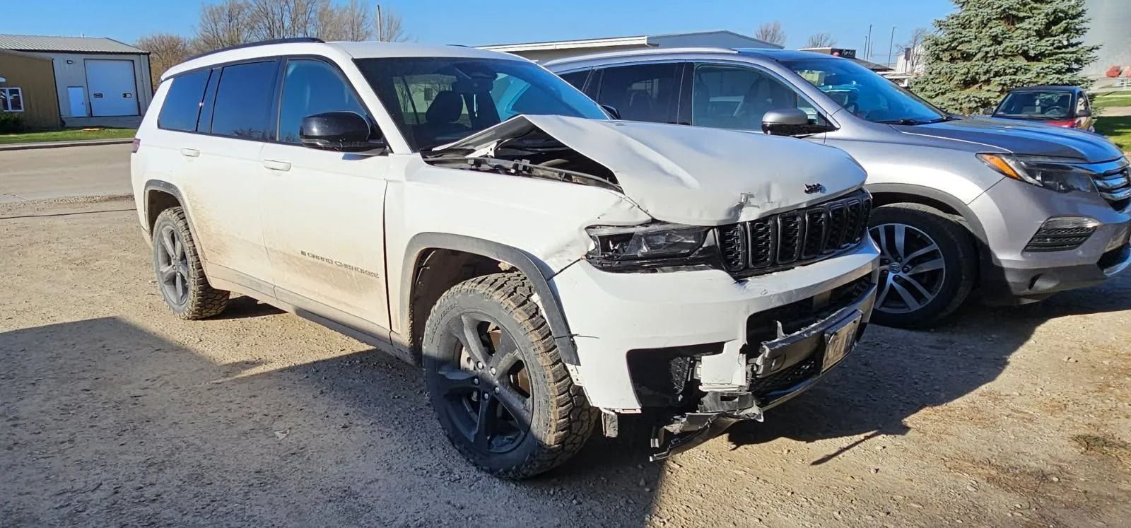 A damaged white SUV with front-end collision; gray SUV behind it on a sunny day.