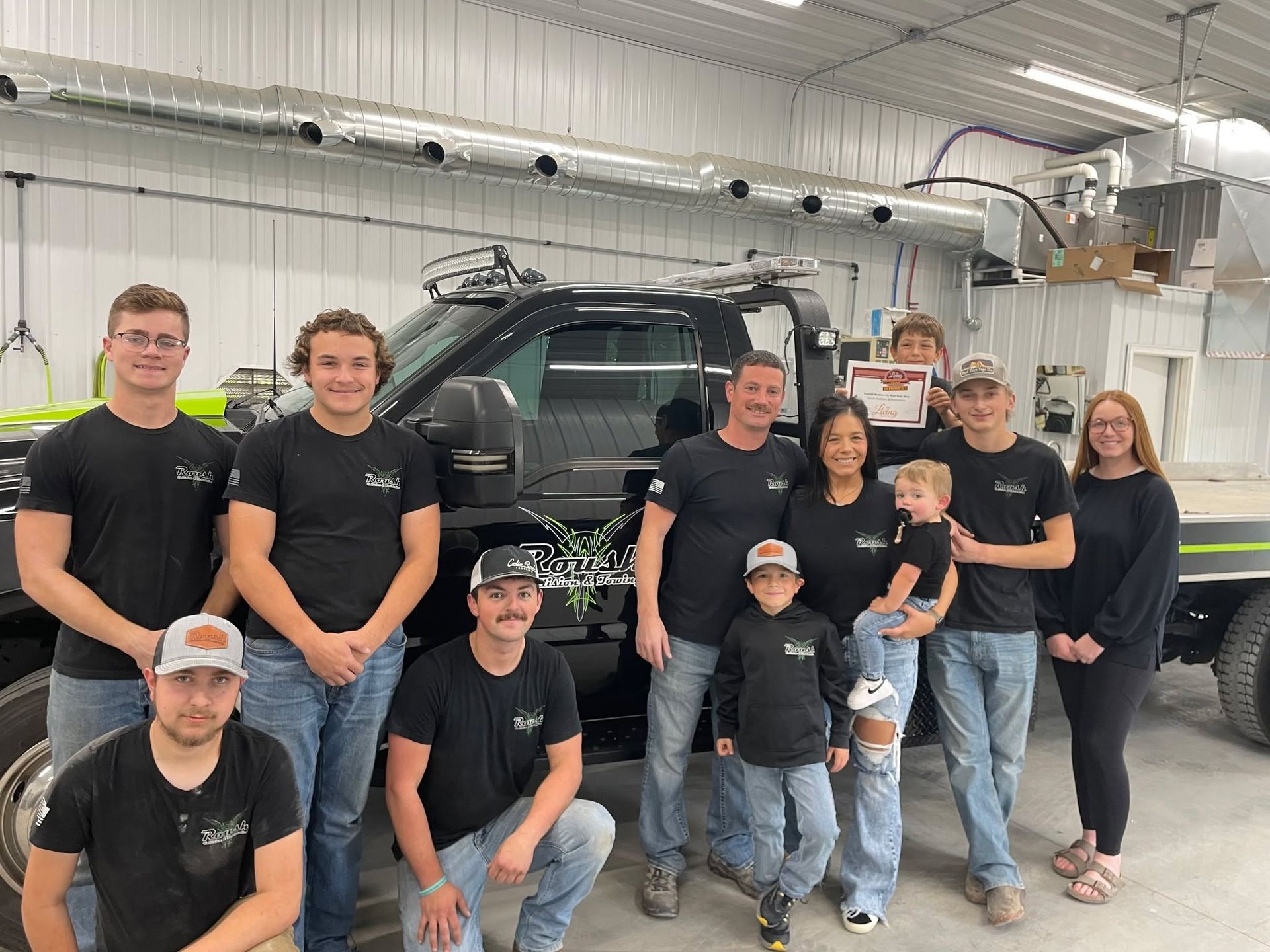 Group of people posing by a black truck in a garage; some are wearing matching shirts.