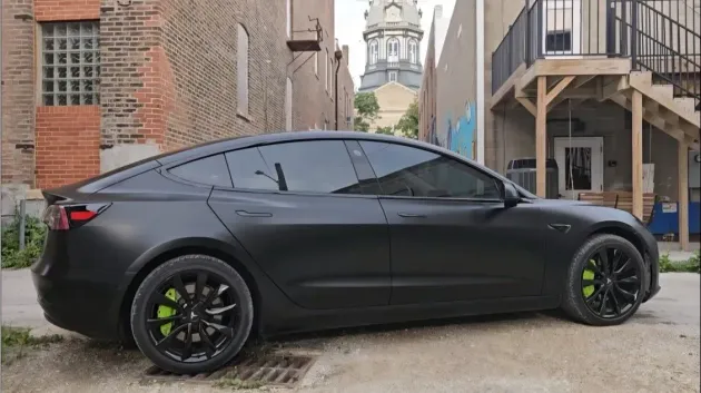 Black Tesla with lime green calipers parked in an alleyway, with a church visible in the background.