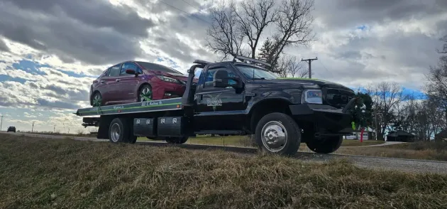 A black tow truck carries a red car on a cloudy day.