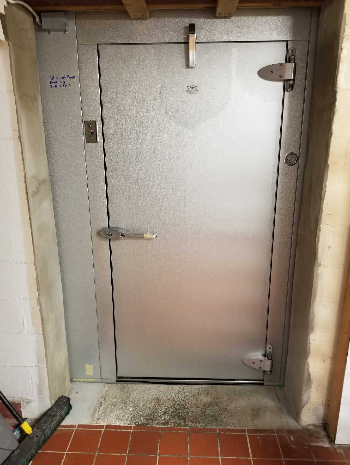 Metal utility door in a concrete wall, with a latch and handle, in a narrow basement-like space.