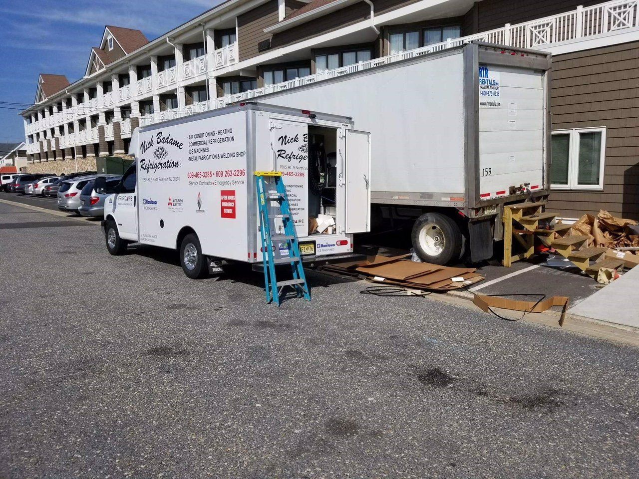 Moving truck and utility van outside apartment buildings, with ladders and construction materials on the ground