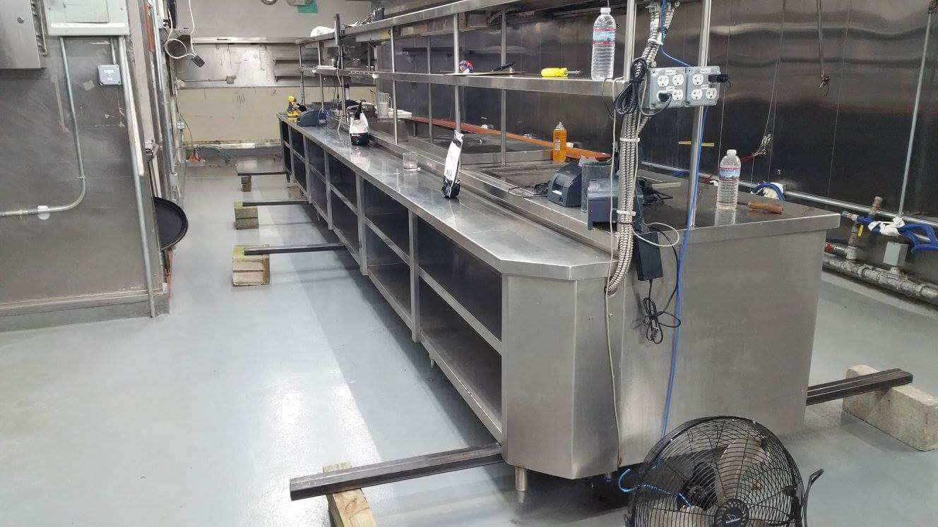 Industrial kitchen prep area with stainless steel counters, sinks, and equipment in a clean workspace