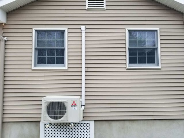 Two beige house windows with a white gutter and an outdoor AC unit below them