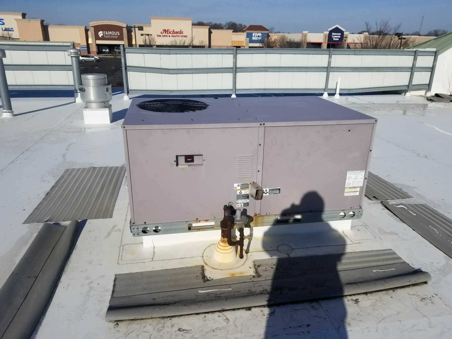 Rooftop HVAC unit beside a white fence, with snow on the roof and a person’s shadow in front.