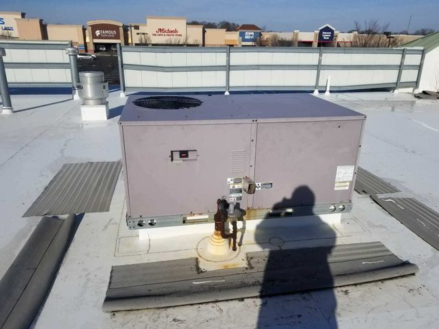 Rooftop HVAC unit beside a fence, with a shadow cast on the snow-covered roof.