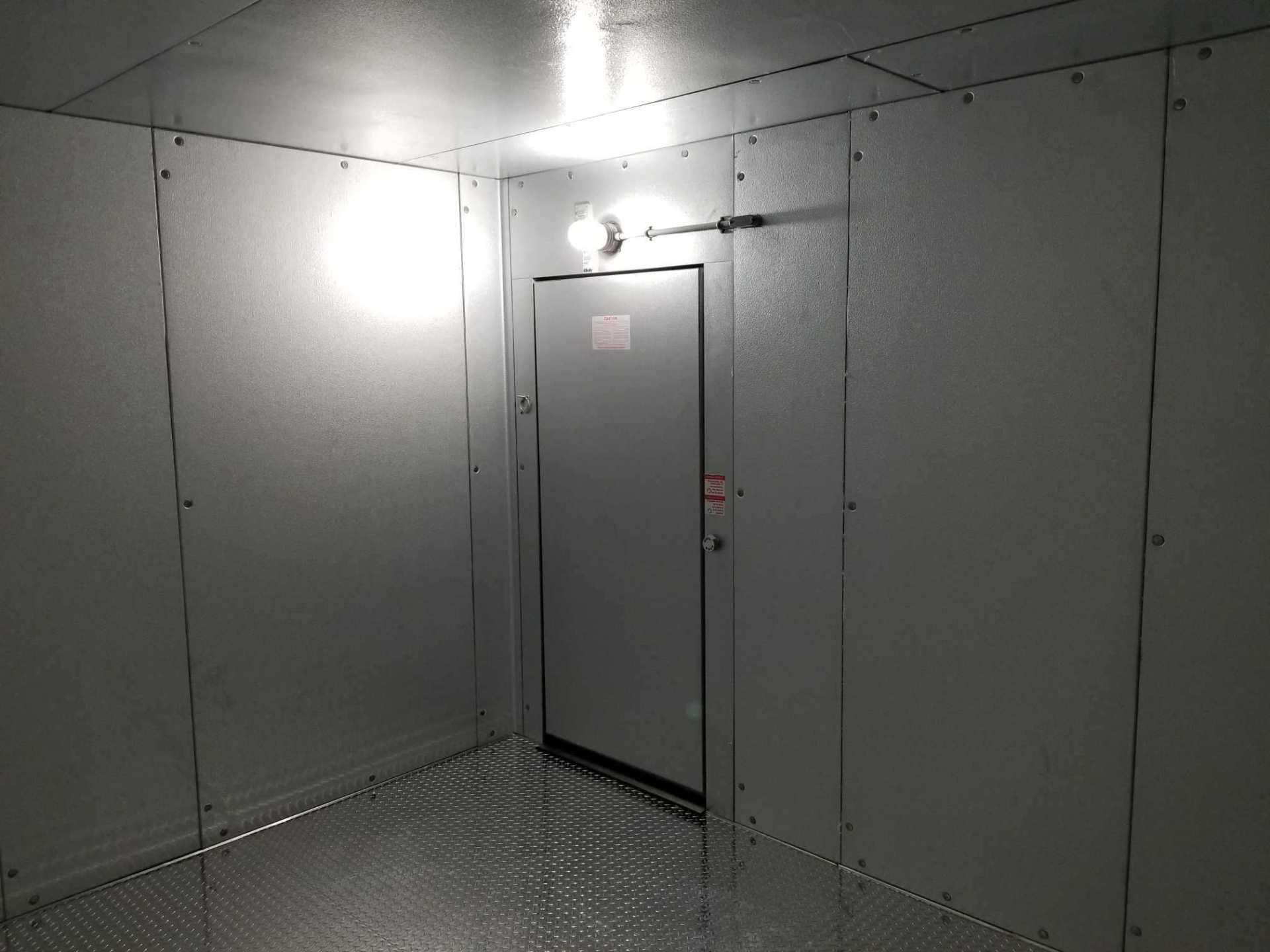 Metal-paneled industrial room with a gray door and bright overhead light.