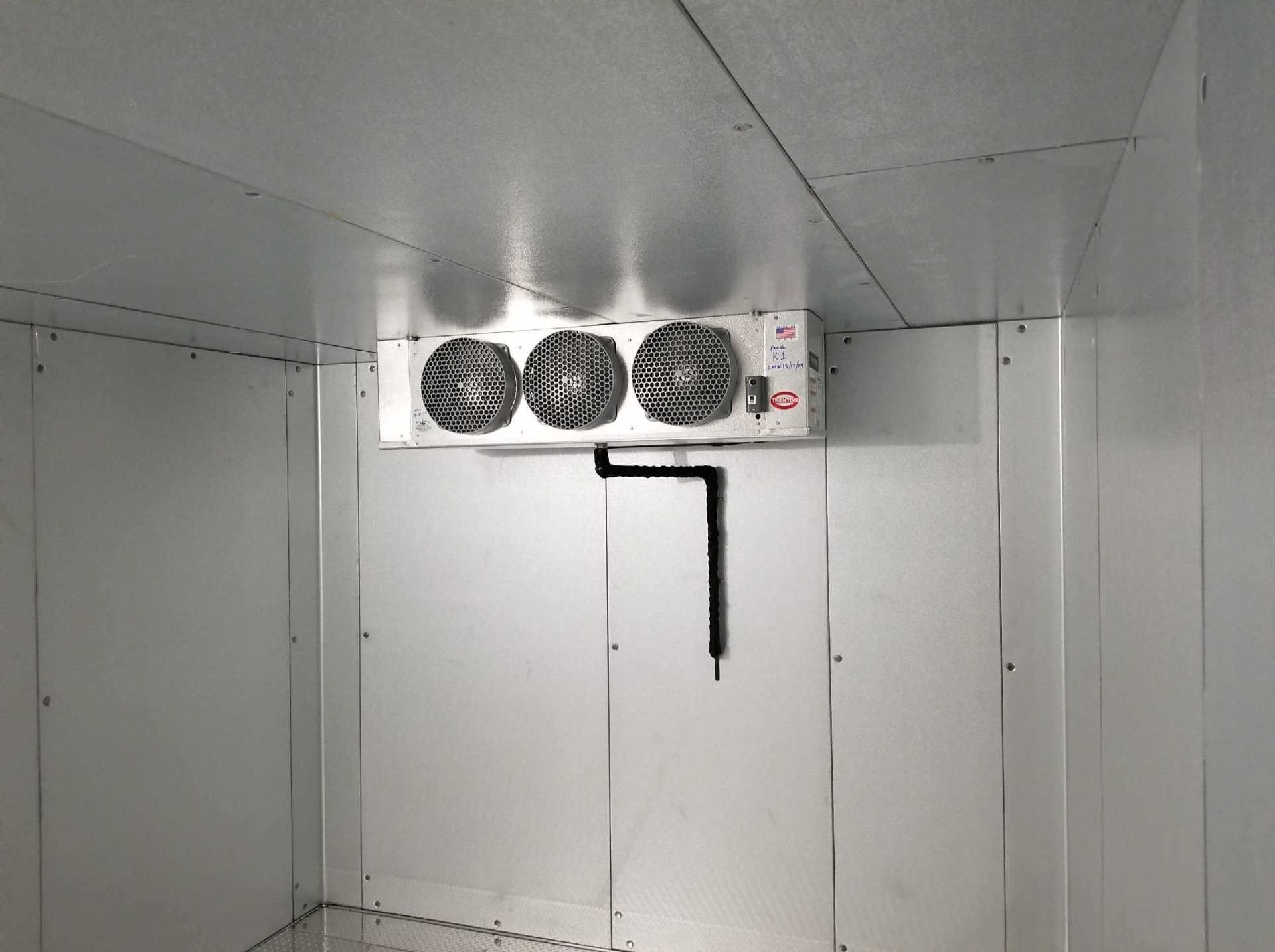 Empty white walk-in cooler with a ceiling-mounted fan unit and hanging black strap.