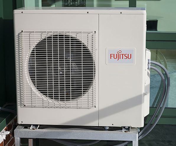 White Fujitsu outdoor air conditioner unit with large fan grille on a metal platform.