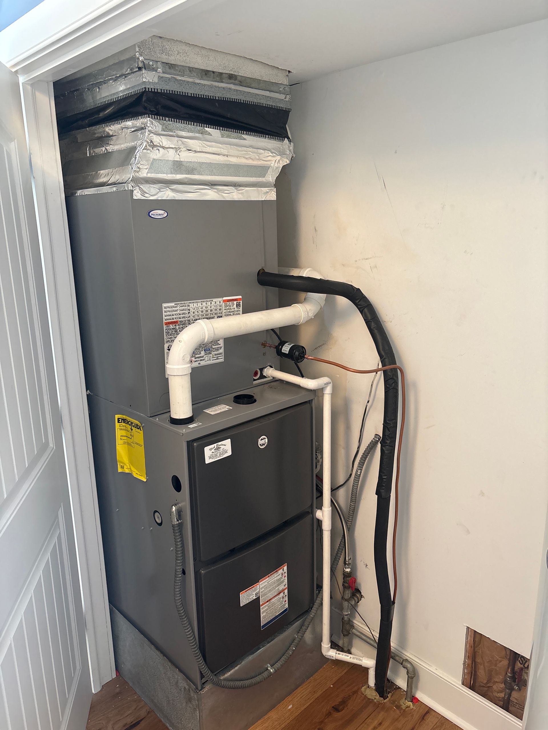 HVAC furnace and ductwork tucked in a small closet with exposed insulated piping.