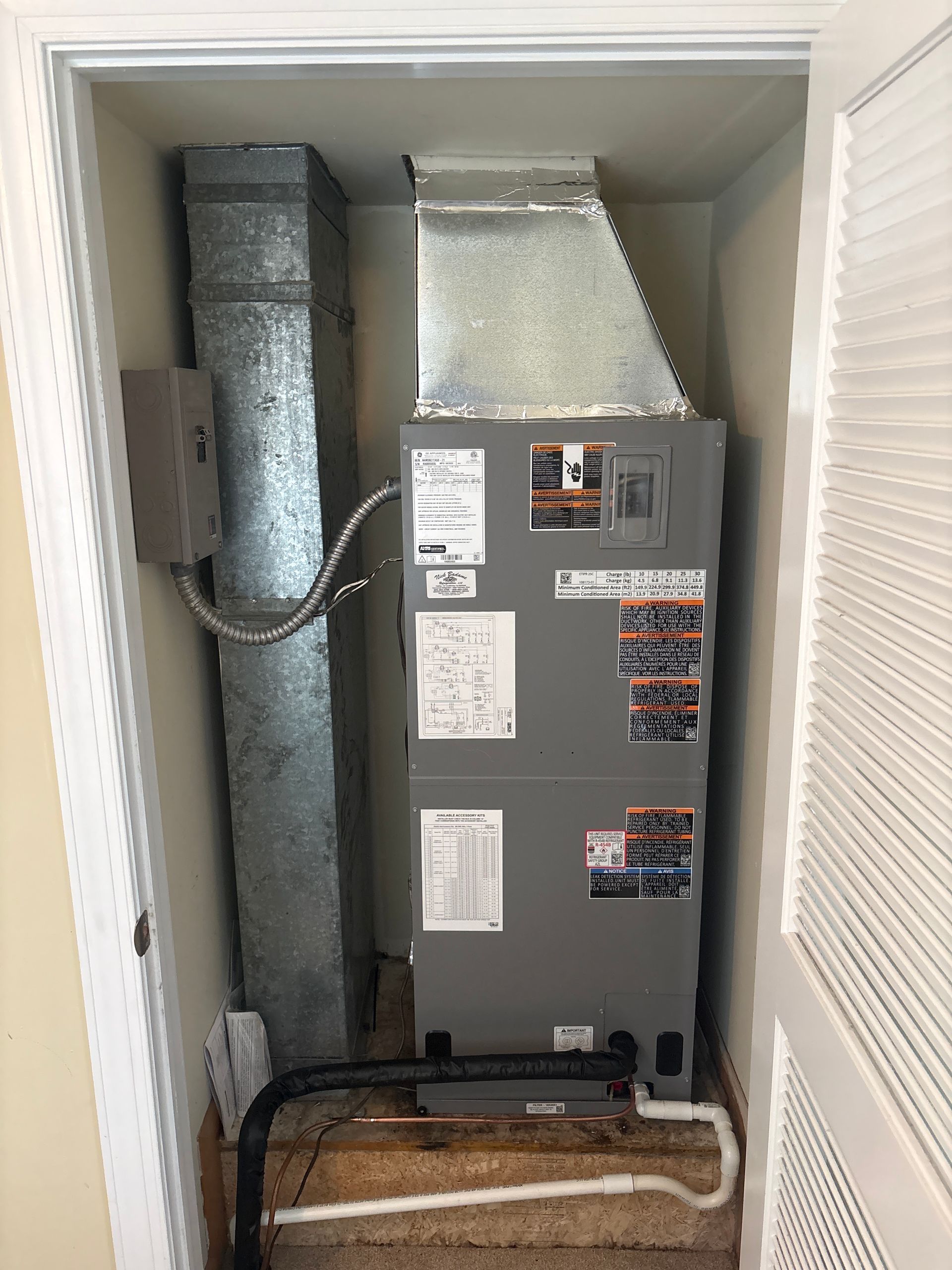 HVAC furnace and ductwork inside a small closet with the access door open