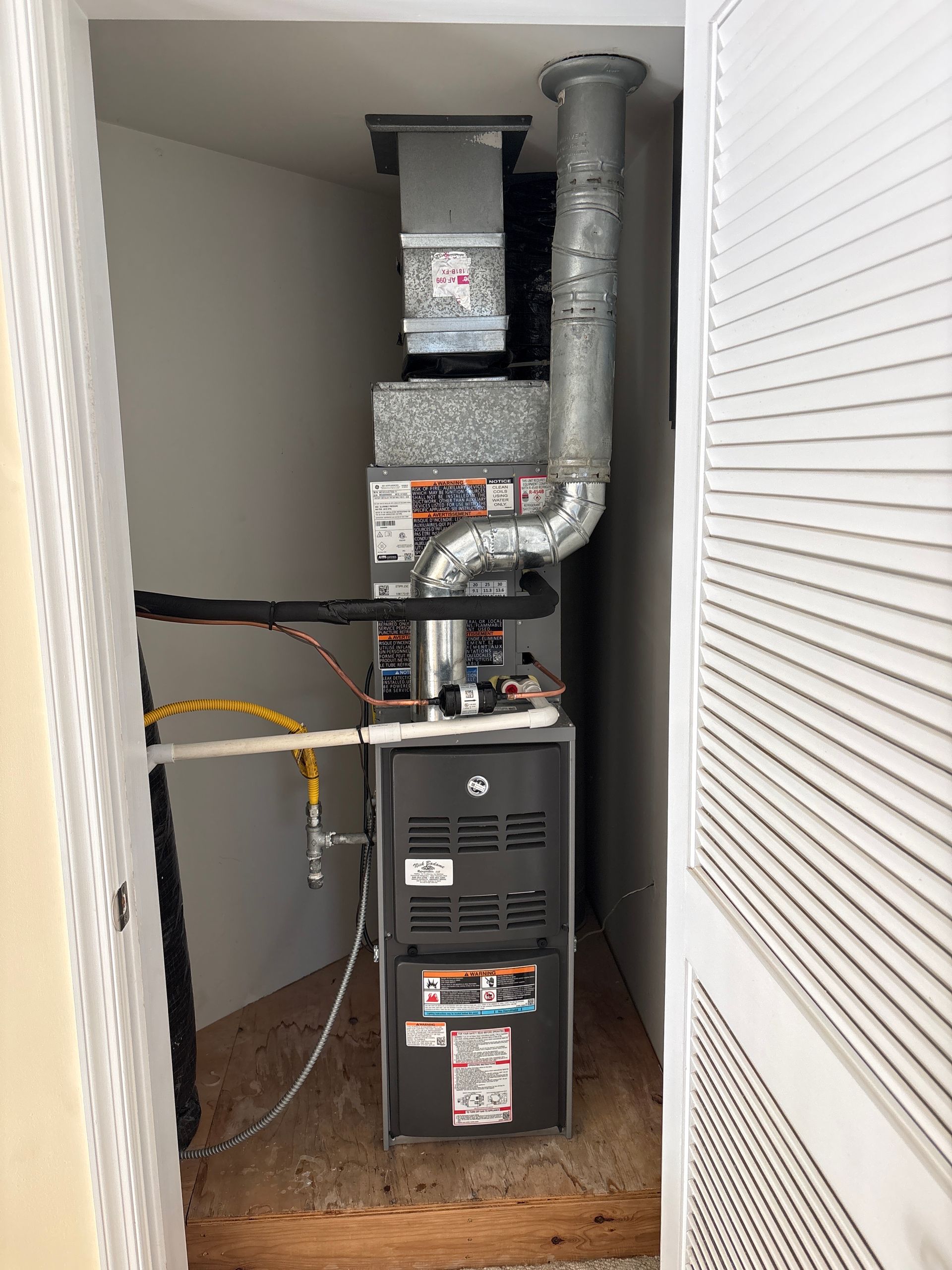 Furnace and ductwork in a small closet, with a yellow cable and white louvered door panels.