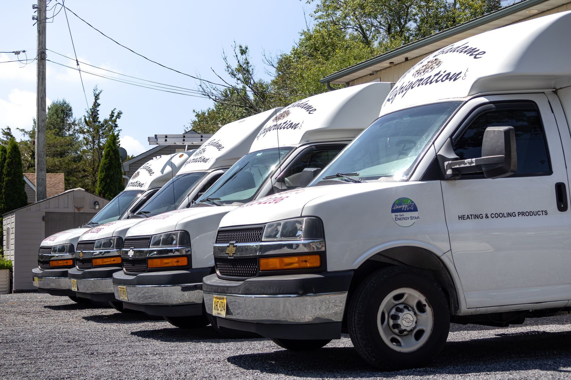 Row of white delivery vans parked on gravel under a sunny sky