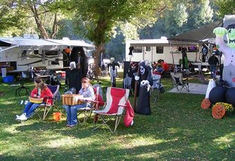 Campground decorated for Halloween. People sit in chairs; RVs and spooky decorations visible.