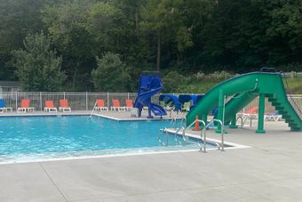 Pool with green and blue slides, lounge chairs, and trees in the background.