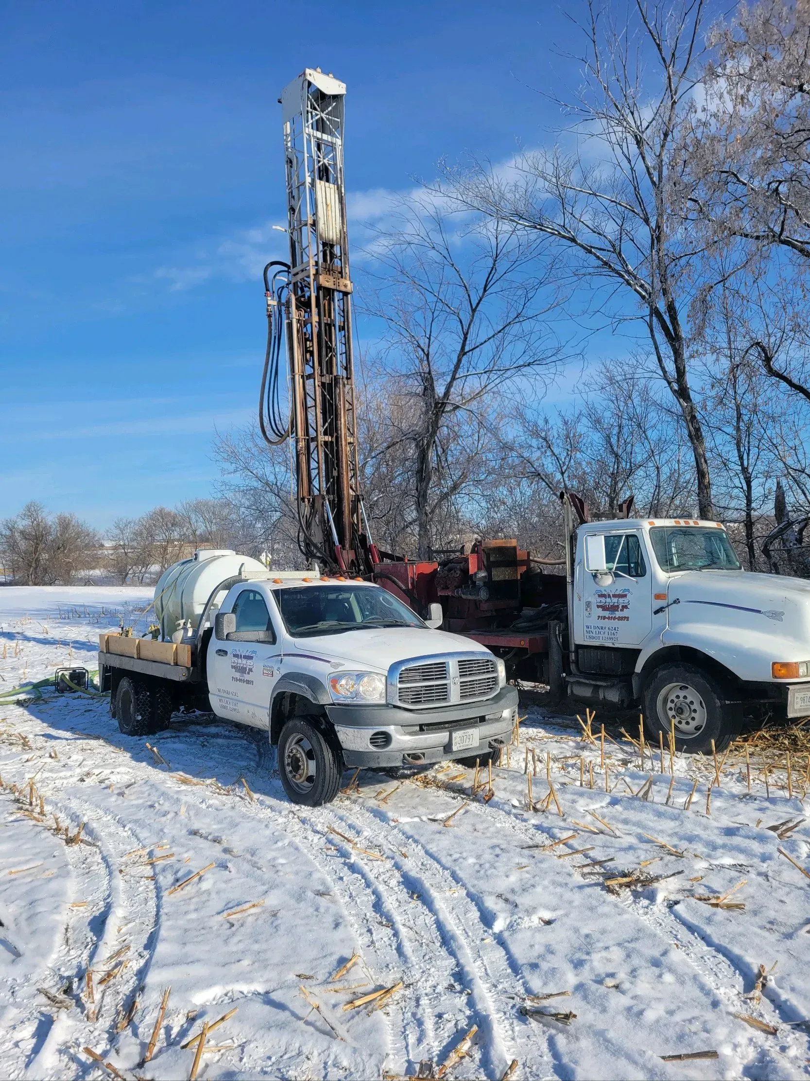 Drilling rig and two trucks in snowy field on a sunny day.