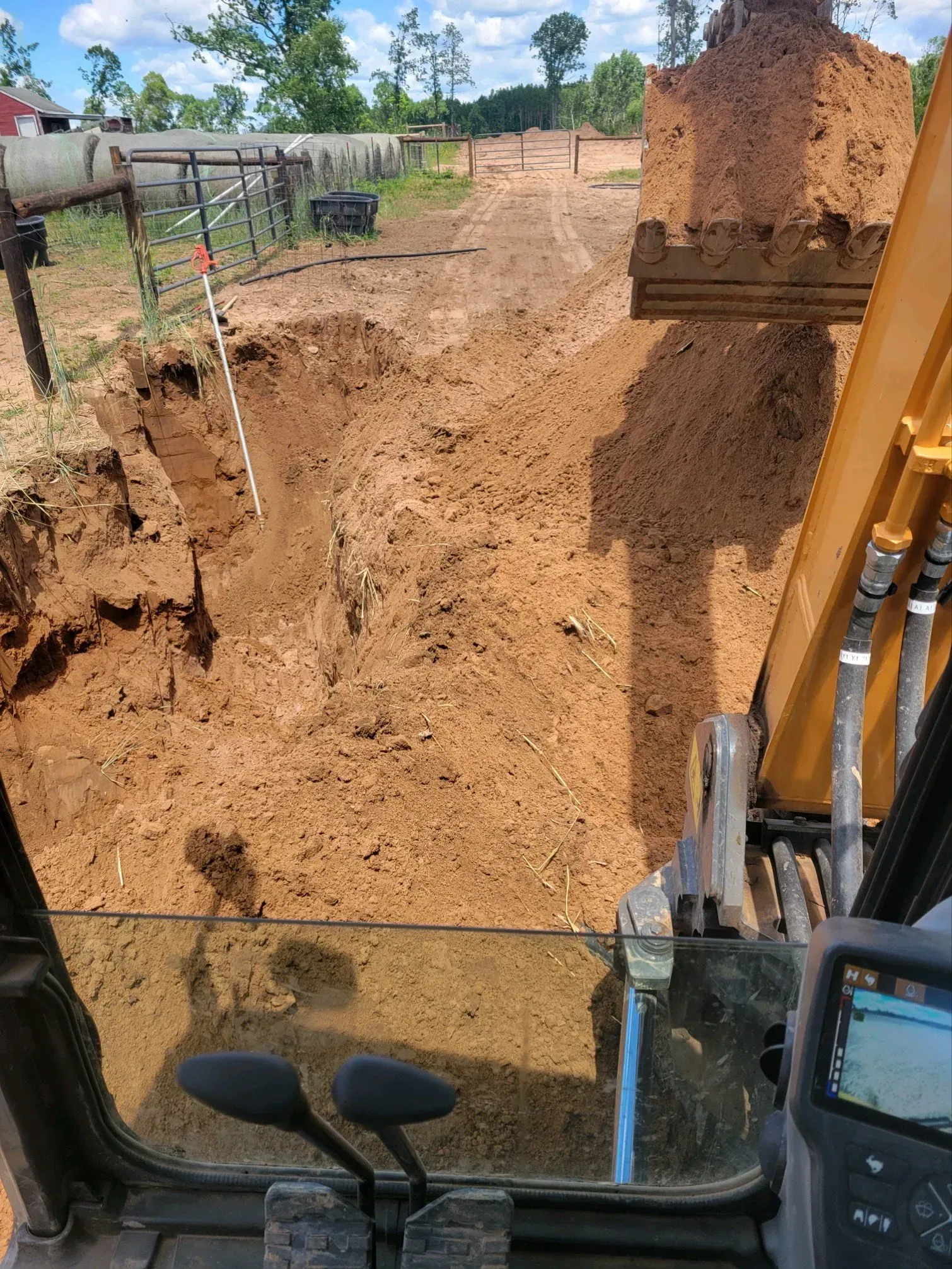 Excavator digging trench in dirt. Brown soil, outdoor rural setting. View from inside the cab.