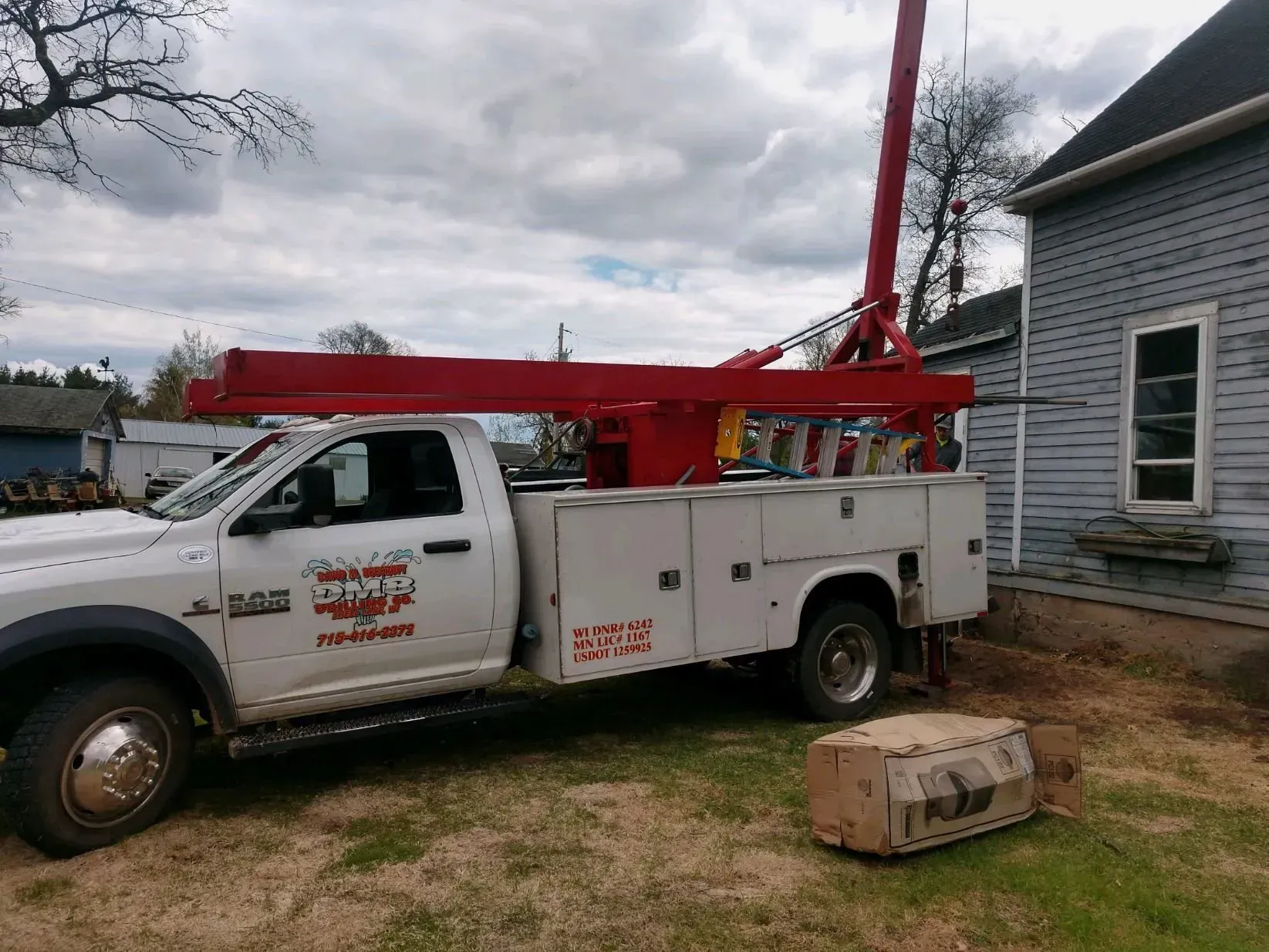 White work truck with a red crane parked next to a house.