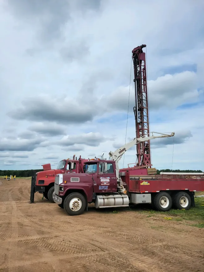 Red drilling rig truck on a dirt road under a cloudy sky.