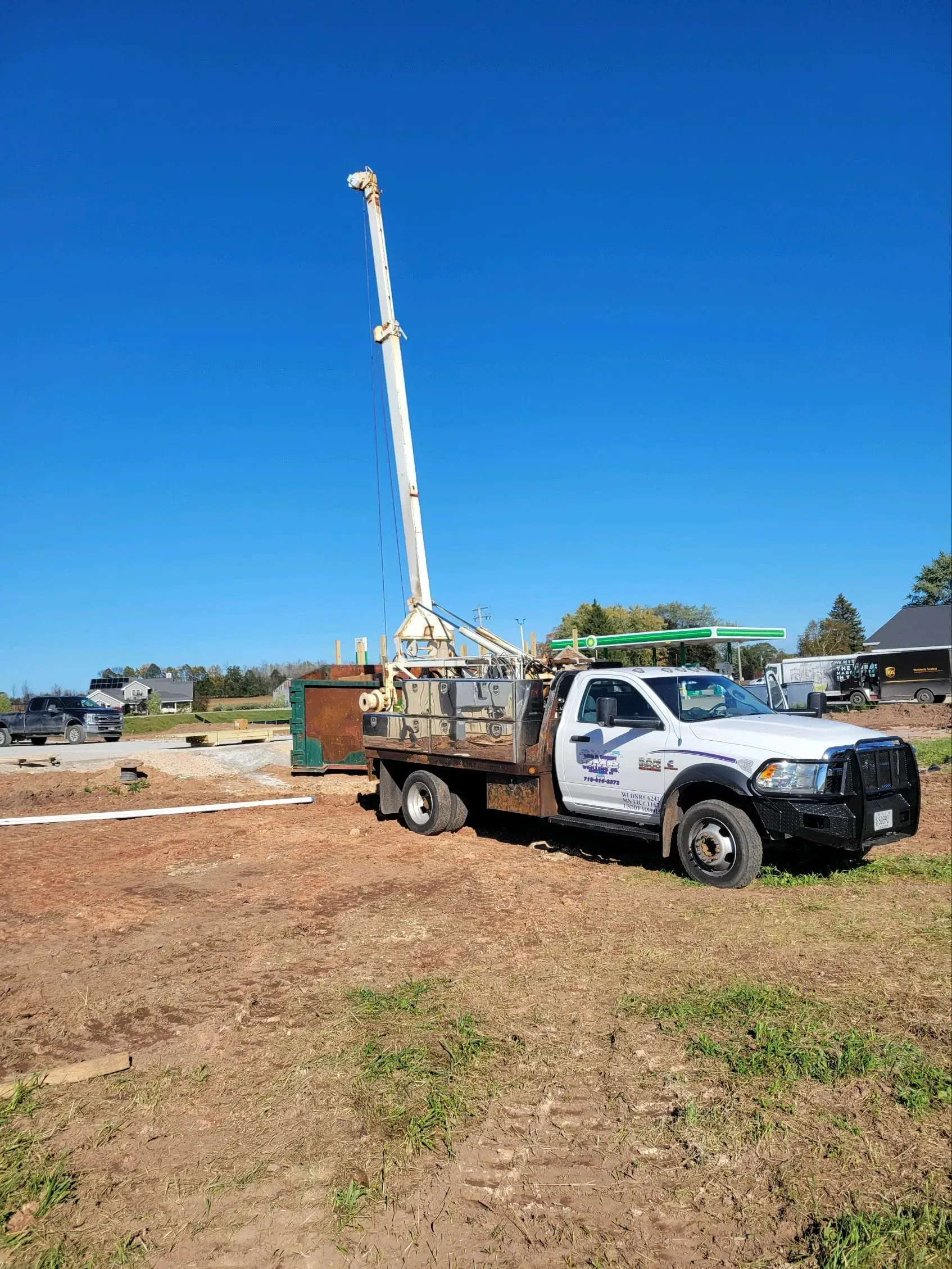 A white truck with a tall crane in a field, under a blue sky, presumably for construction.