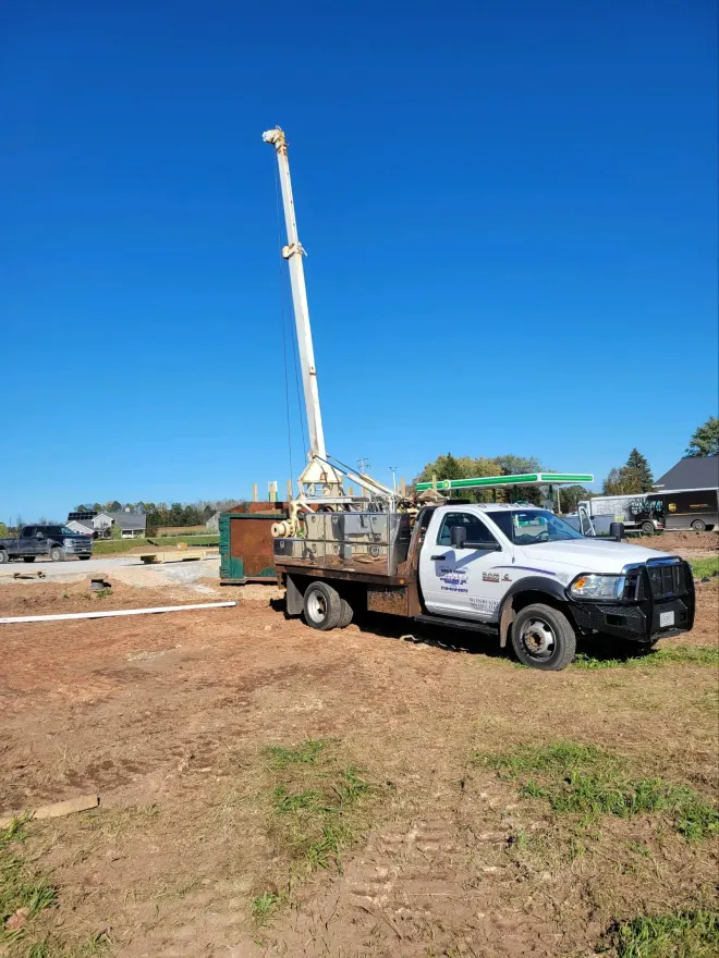 A white truck with a crane in a dirt field under a blue sky.