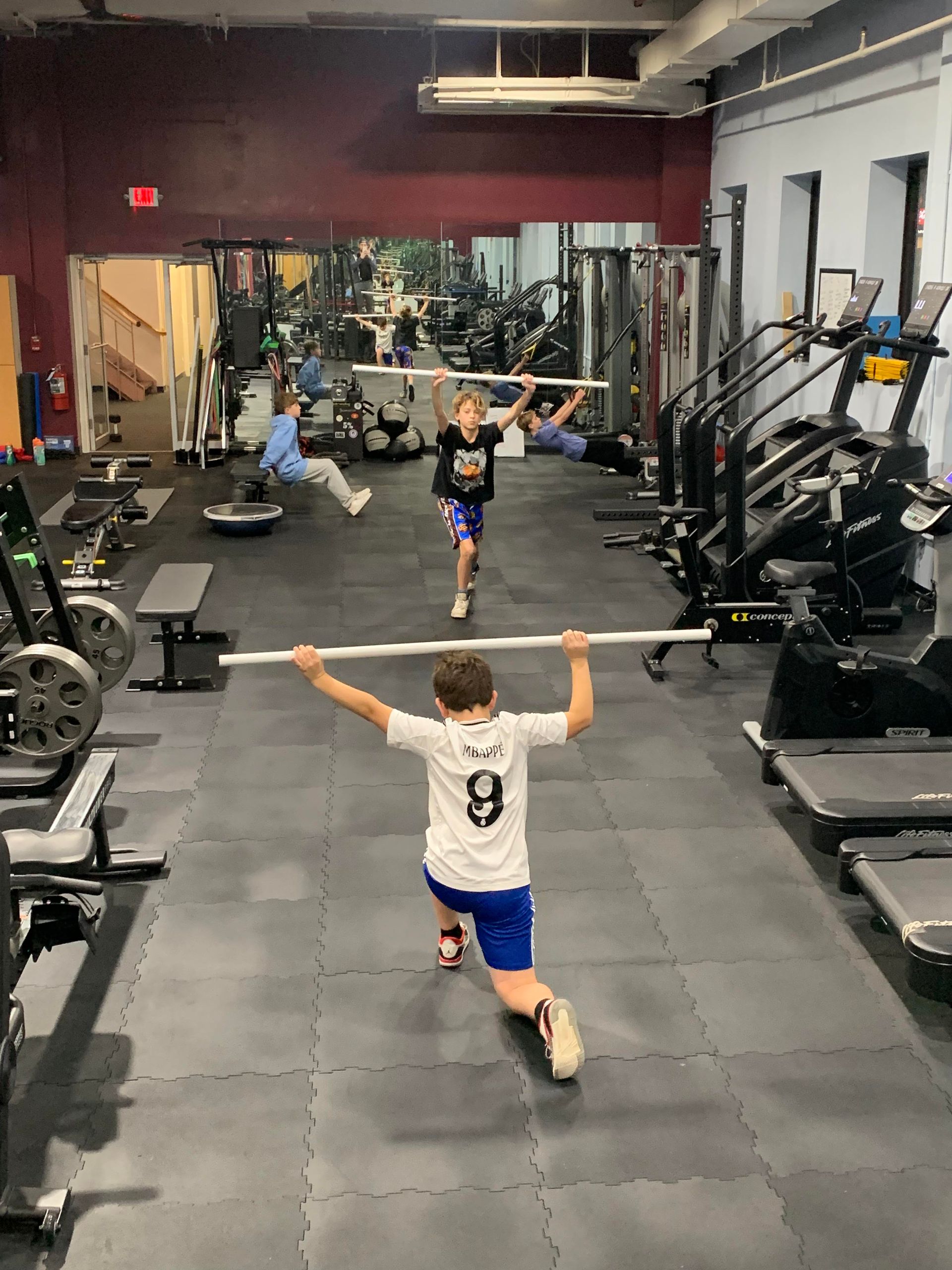 A boy is holding a barbell over his head in a gym.