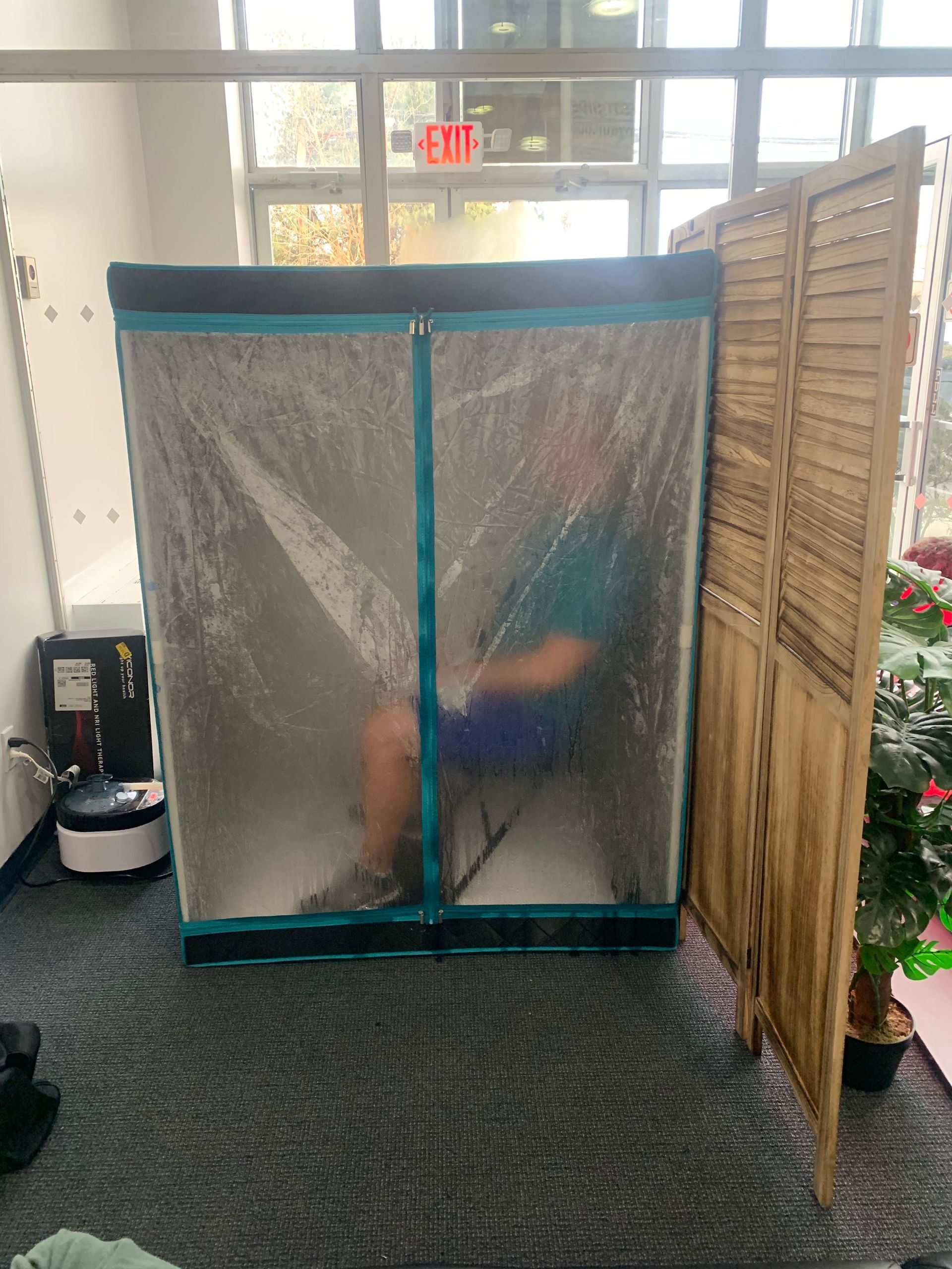 A man is sitting in a plastic covered room next to a wooden divider.