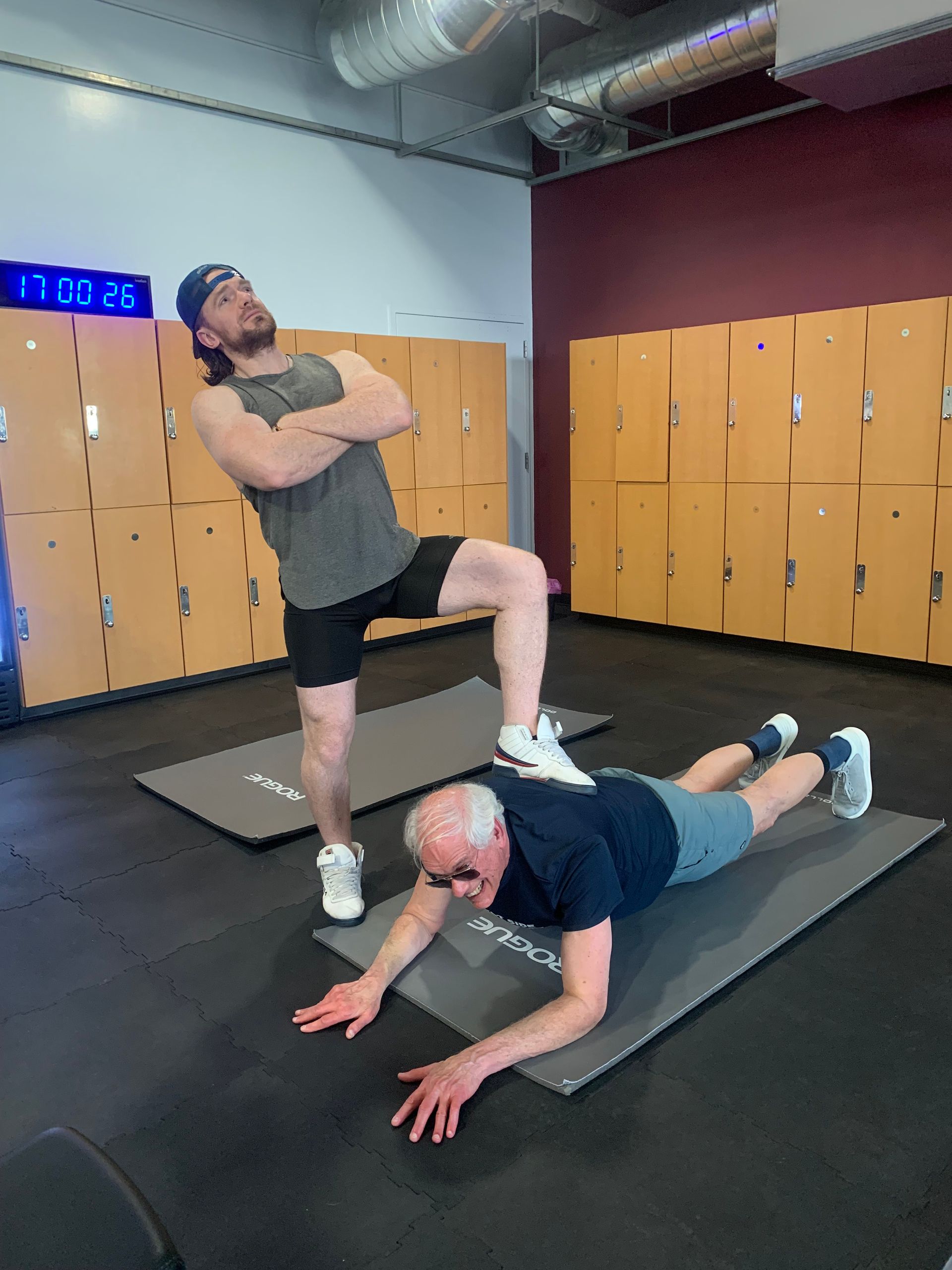 Two men are doing exercises on mats in a gym.