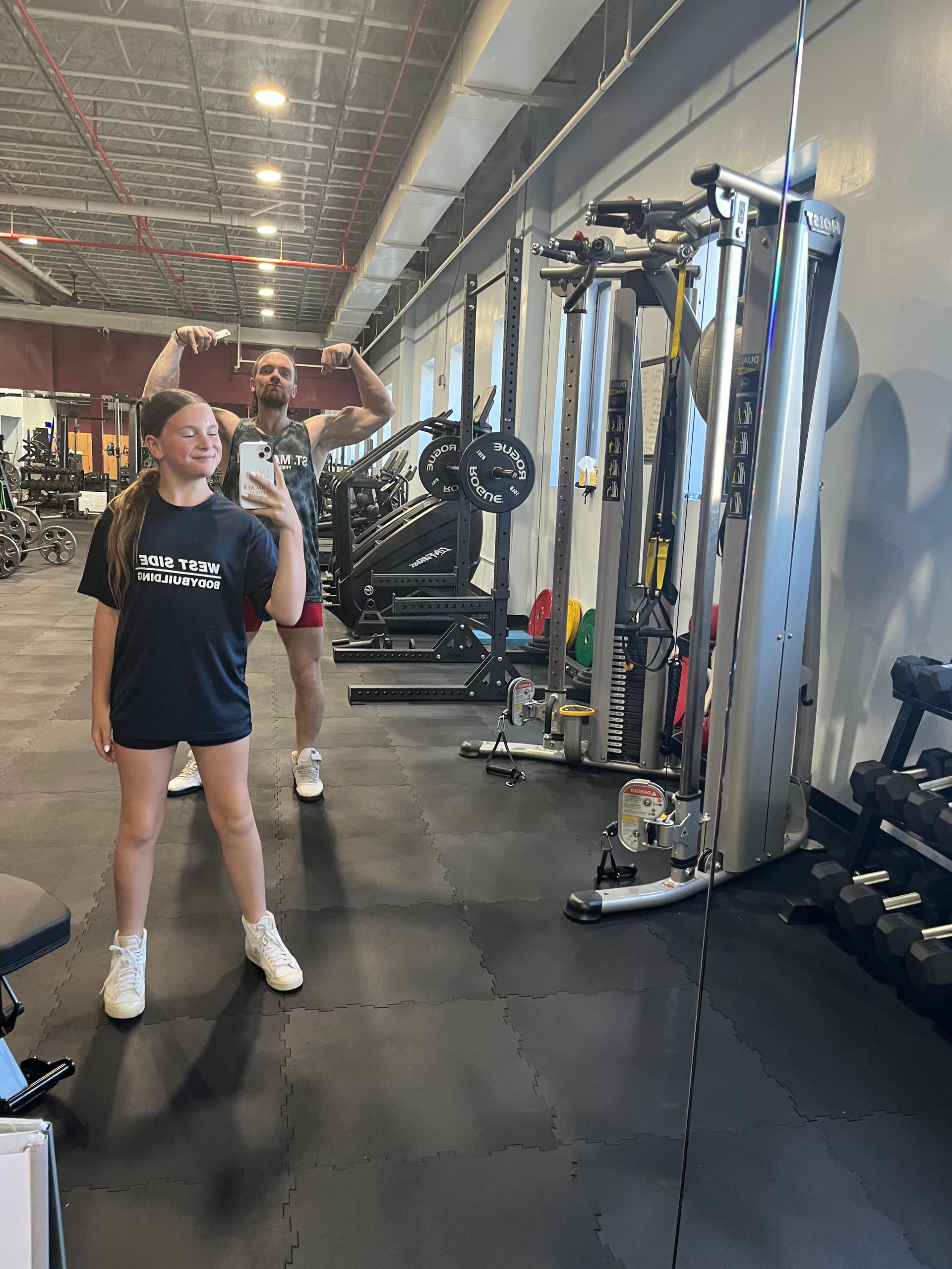 A man and a girl are taking a selfie in a gym.