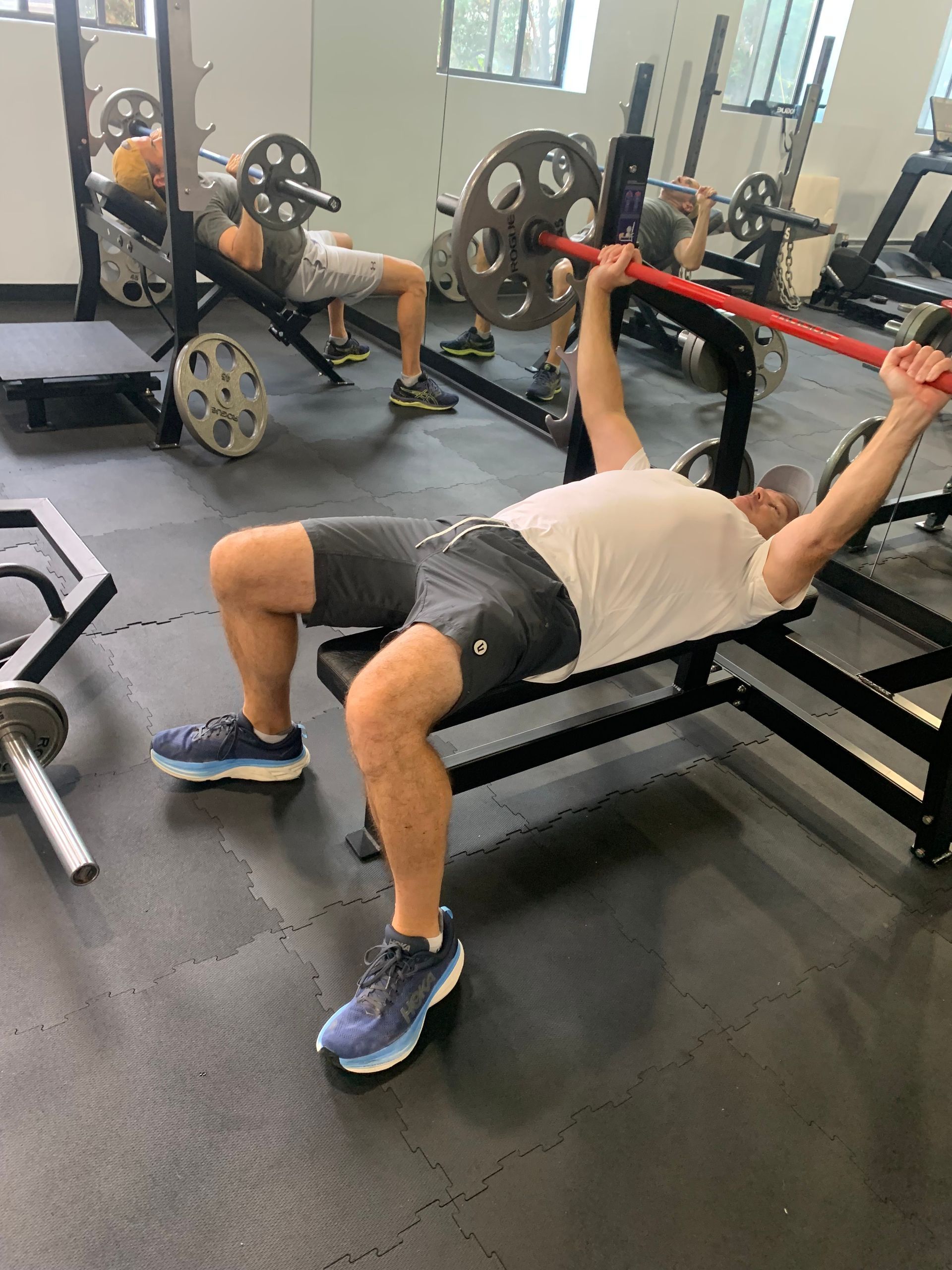 A man is lifting a barbell on a bench in a gym.