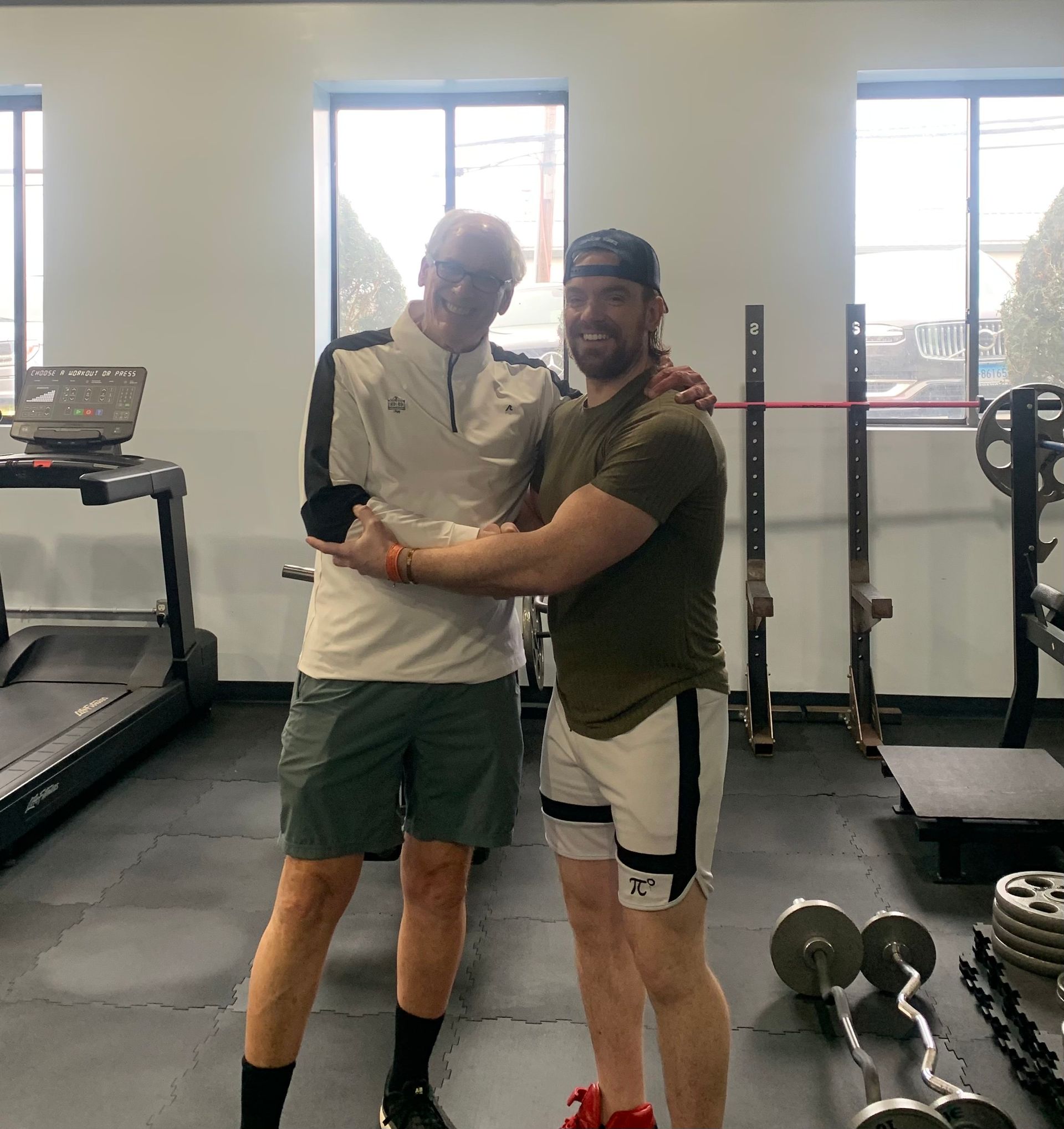 Two men are posing for a picture in a gym.