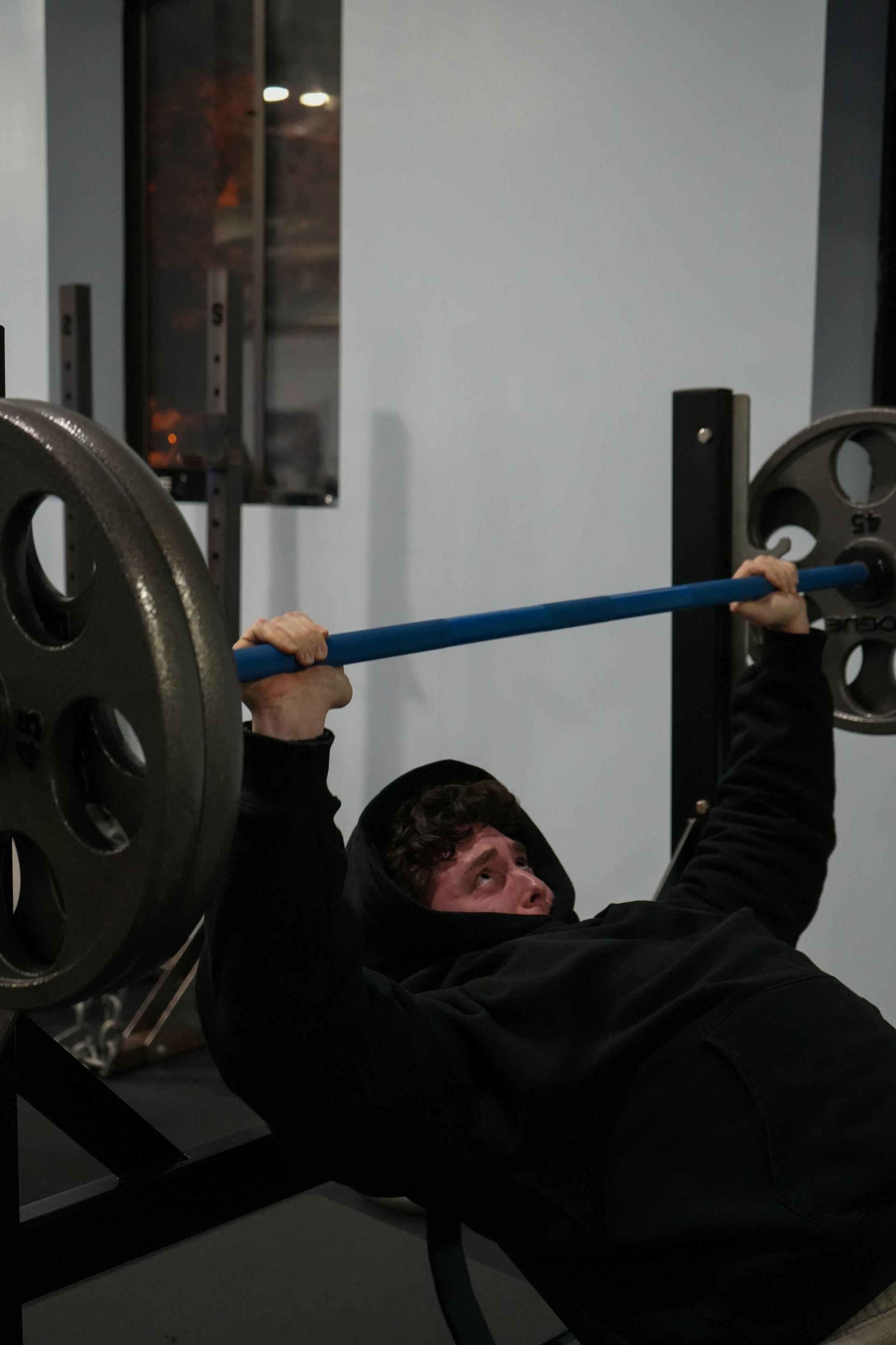 A man is lifting a barbell on a bench in a gym.