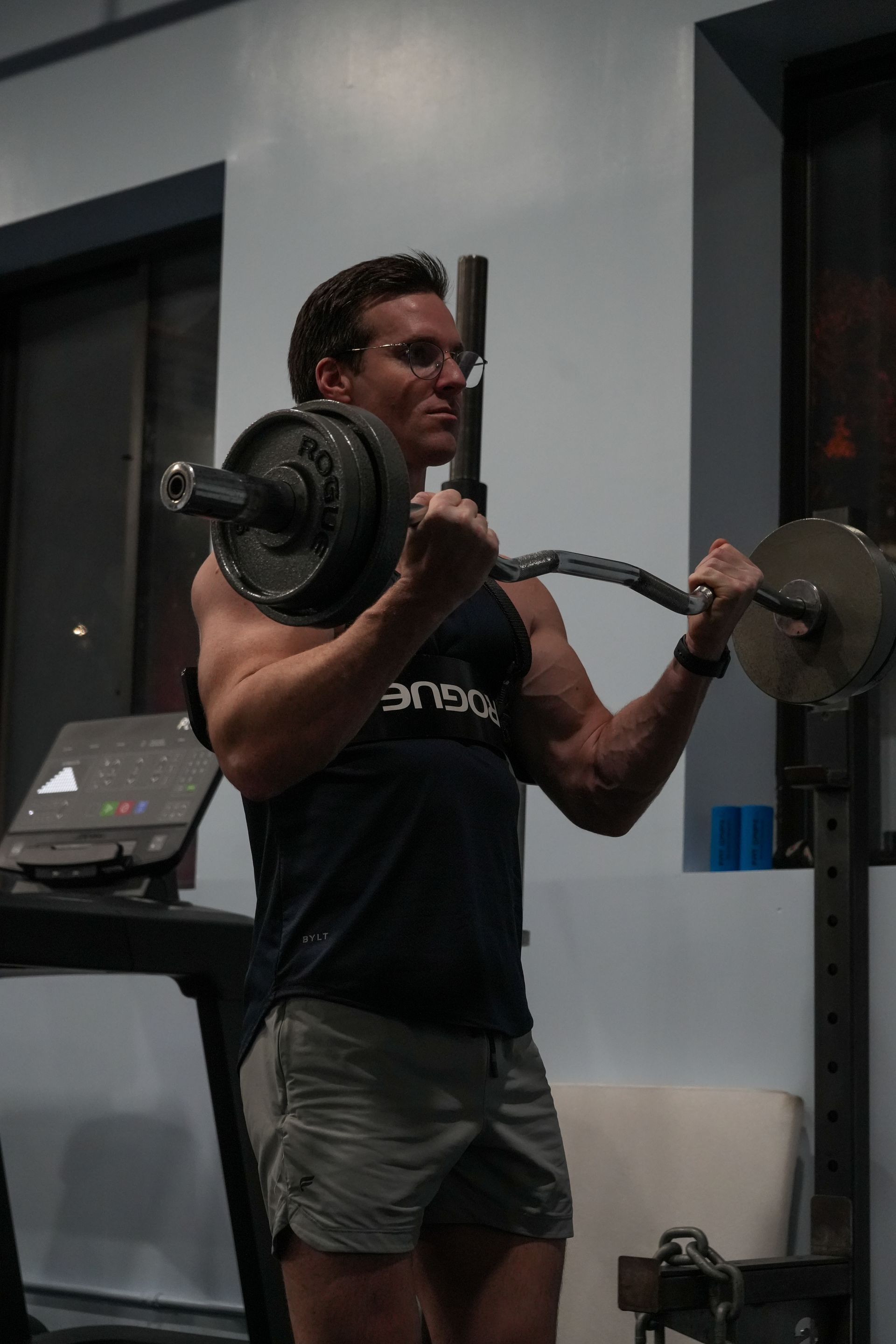 A man in a black tank top is lifting a barbell in a gym.