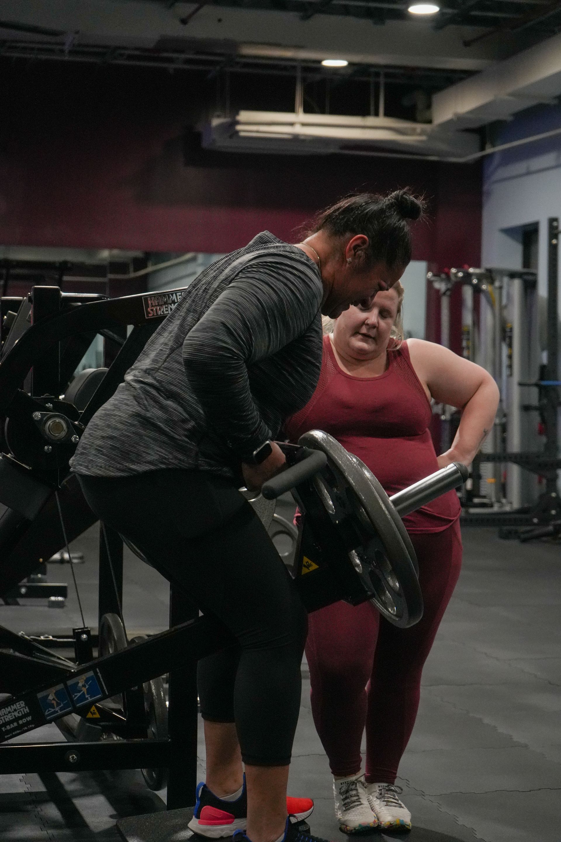 A man is helping a woman lift a barbell in a gym.