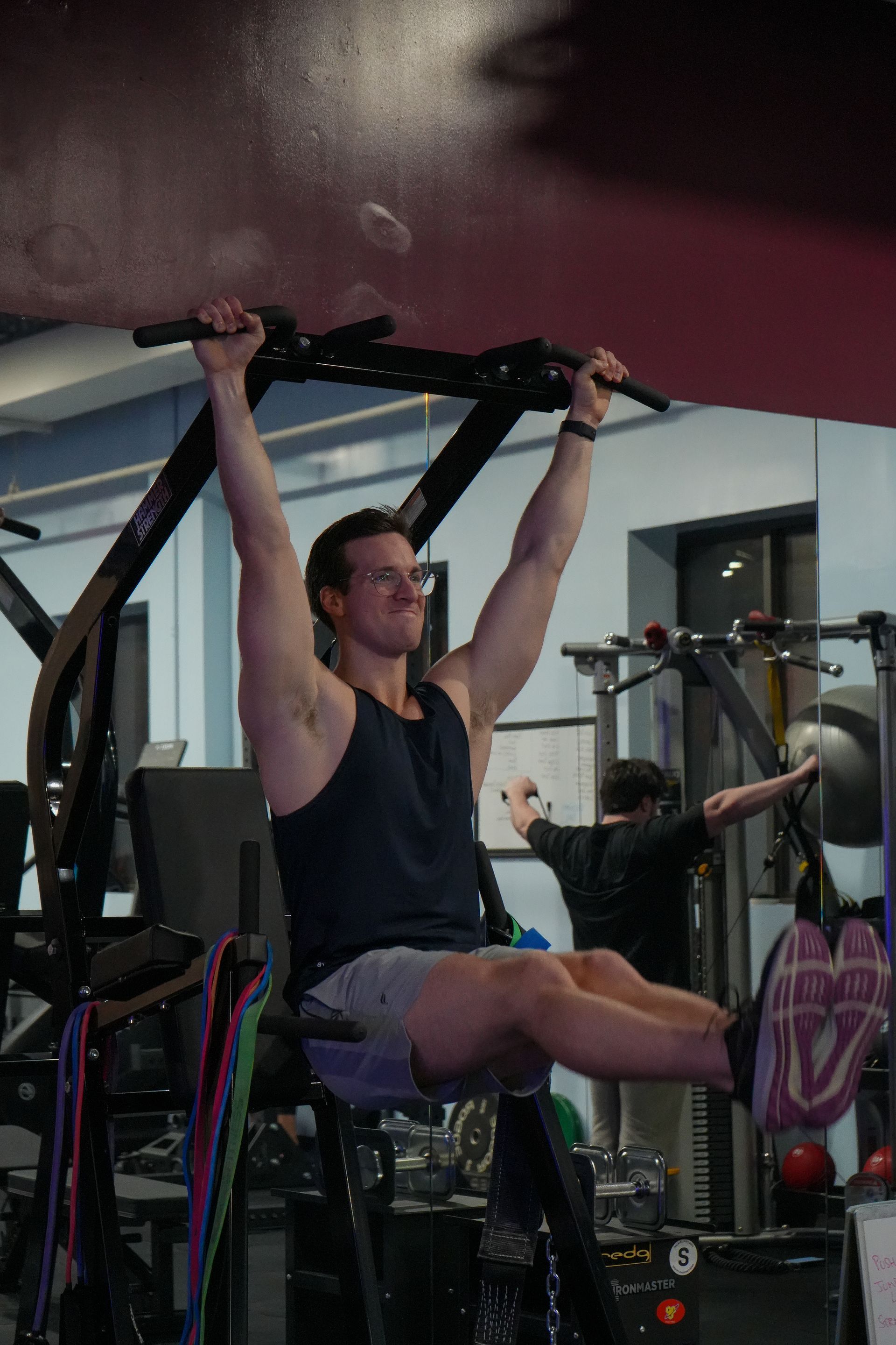 A man is doing pull ups on a machine in a gym.