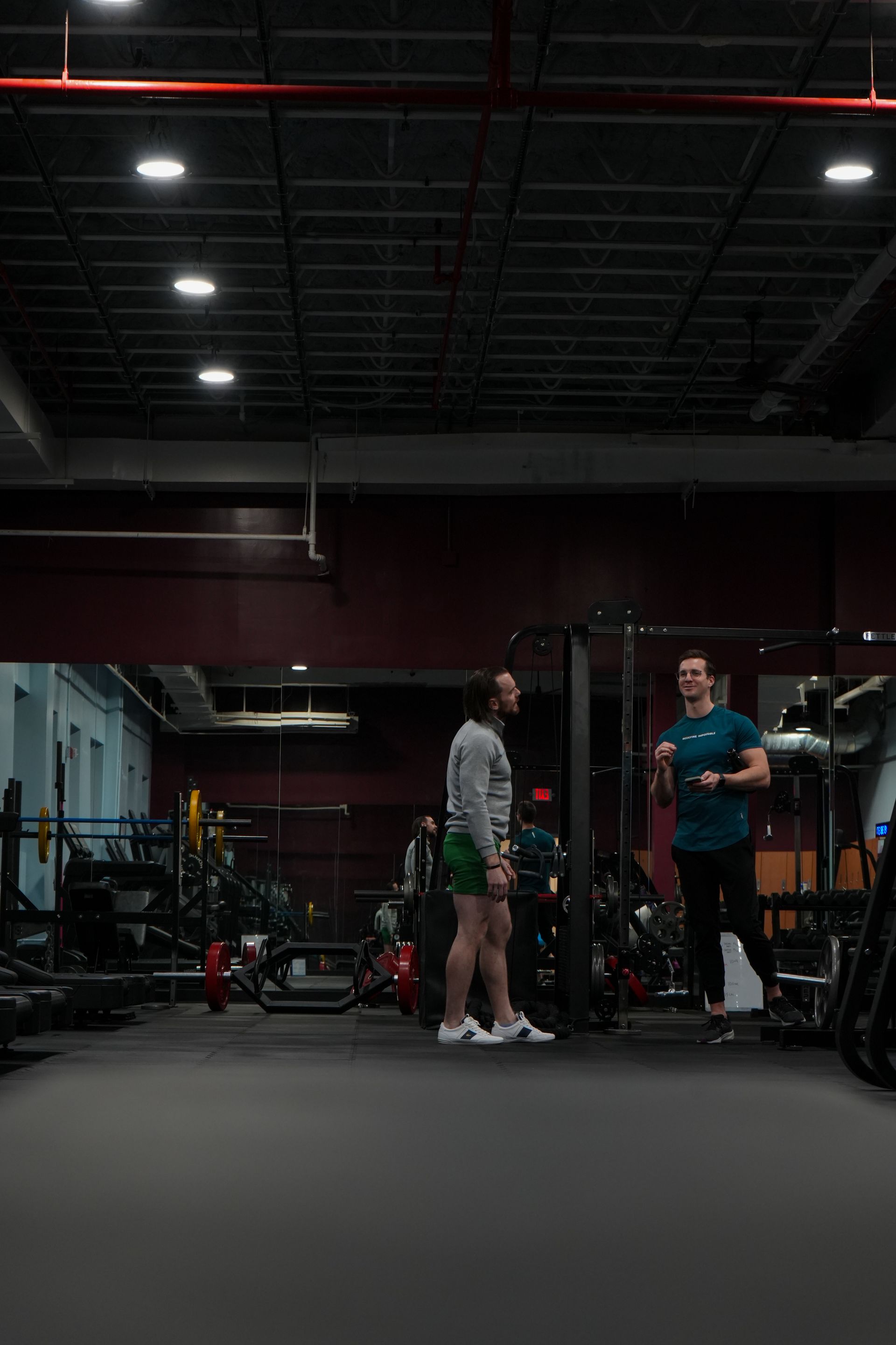 Two people are standing in a gym talking to each other.