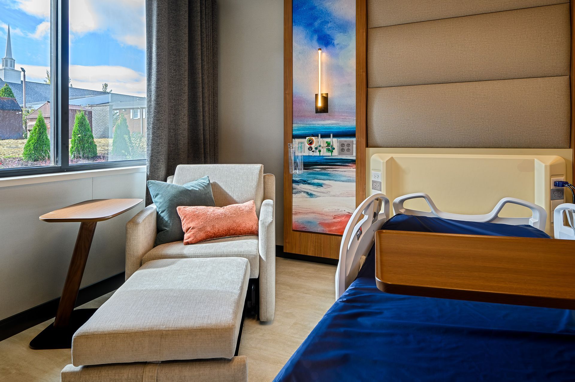 A hospital room with blue beddings and a brown couch