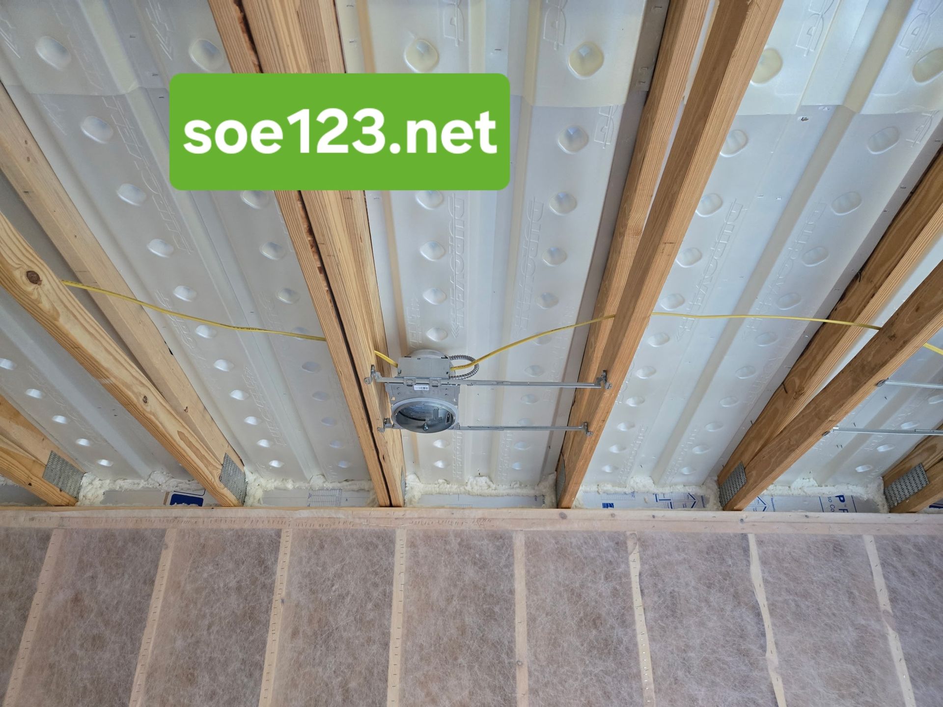 Wood ceiling joists with insulation, electrical box, and insulated wall below.