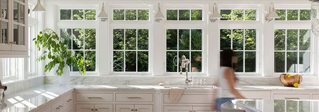 White kitchen with large windows, greenery outside, and a person moving in the background.