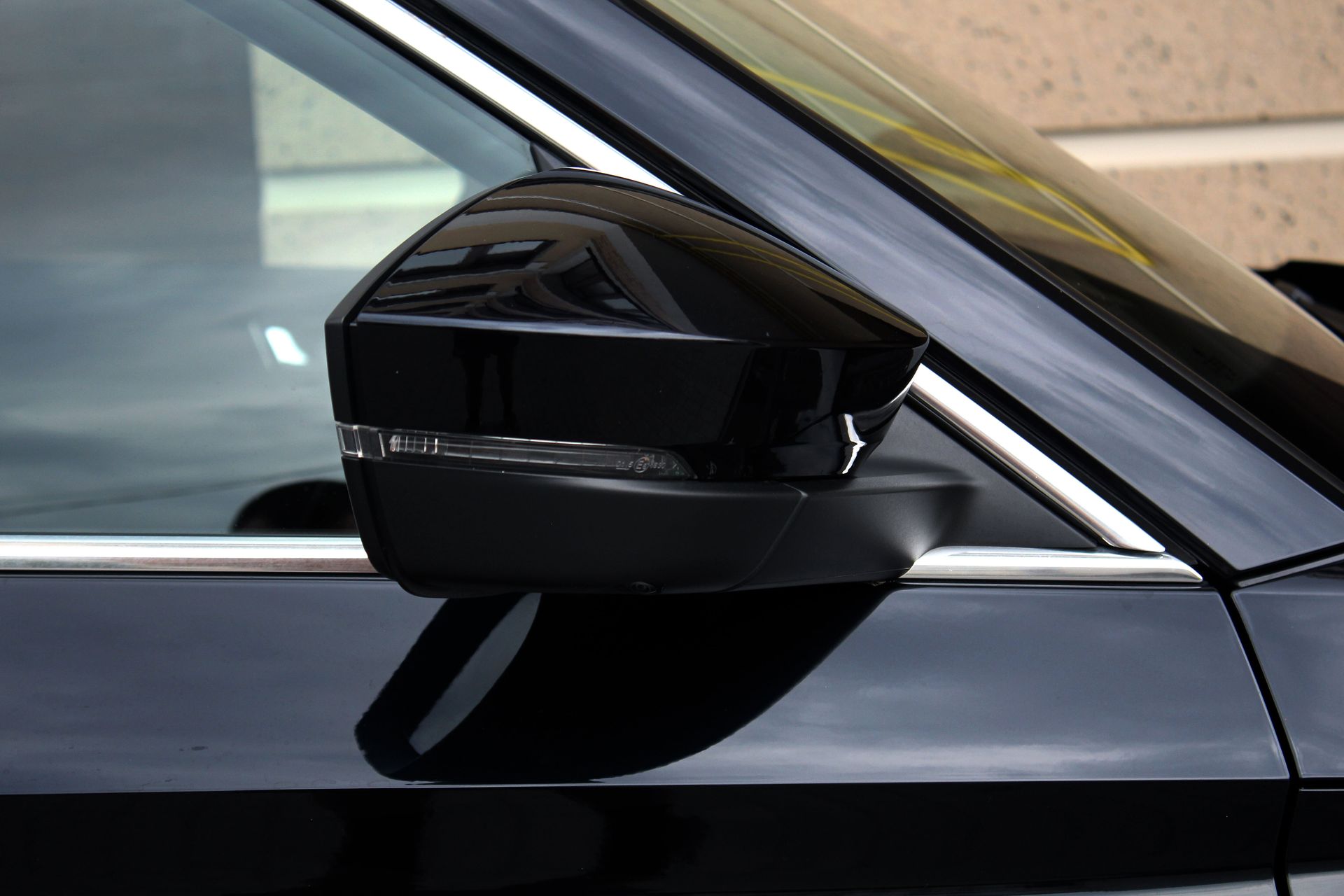Black car side mirror, angled up, reflecting the environment.