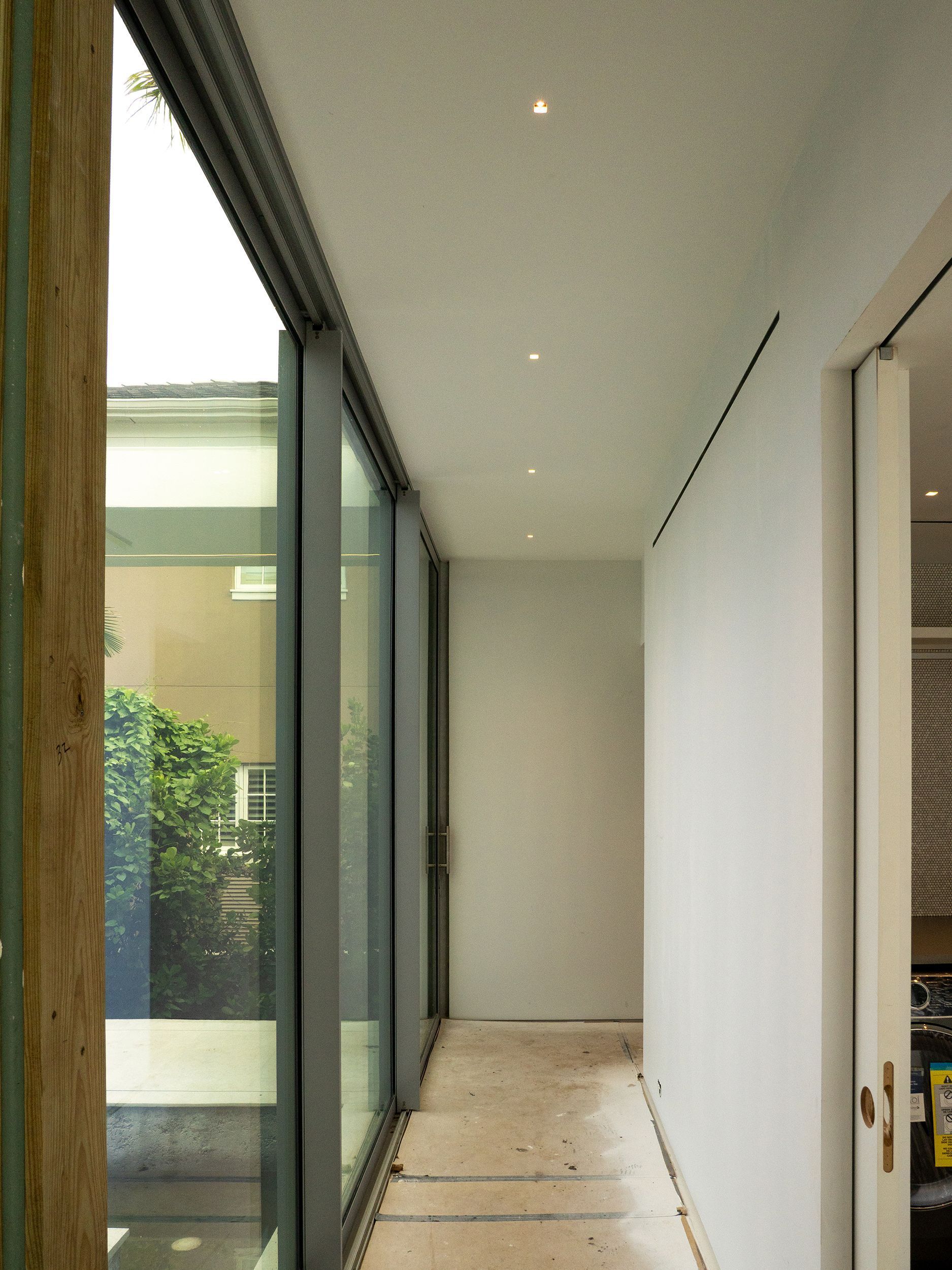 Narrow interior hallway with sliding glass doors on the left, white walls, and recessed ceiling lights.
